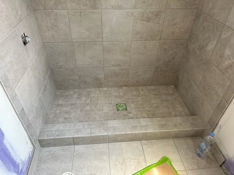A bathroom with a tiled shower stall and a green mat on the floor.