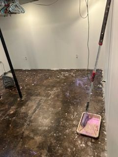 A room with a bucket of paint and a roller on the floor.