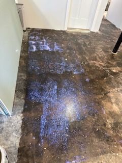 A person is standing on a dirty floor next to a refrigerator.