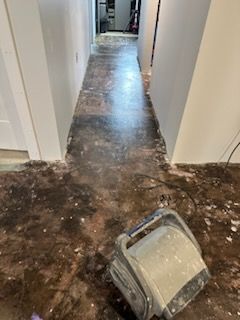 A vacuum cleaner is sitting on a dirty floor in a hallway.