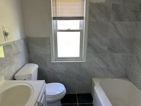 A bathroom with a toilet , sink , tub and window.