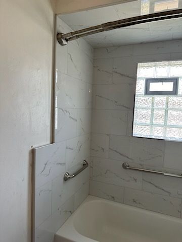 A bathroom with a tub , shower and mirror.