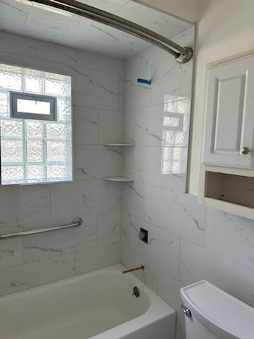 A bathroom with a tub , toilet , shower and window.