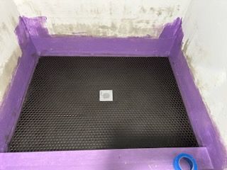 A purple tape is being used to seal a shower floor.
