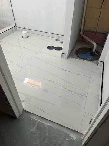A bathroom with a white tile floor and a drain.
