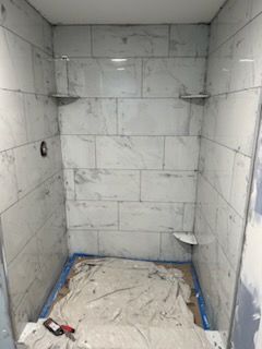 A bathroom with white tiles and a blue tarp on the floor.