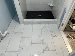 A bathroom with white tiles and a black shower stall.