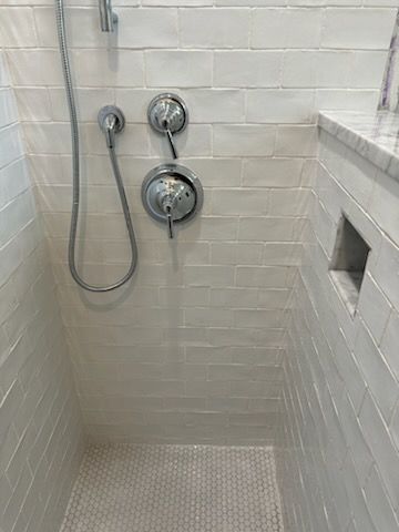 A shower with white tiles and a chrome shower head.