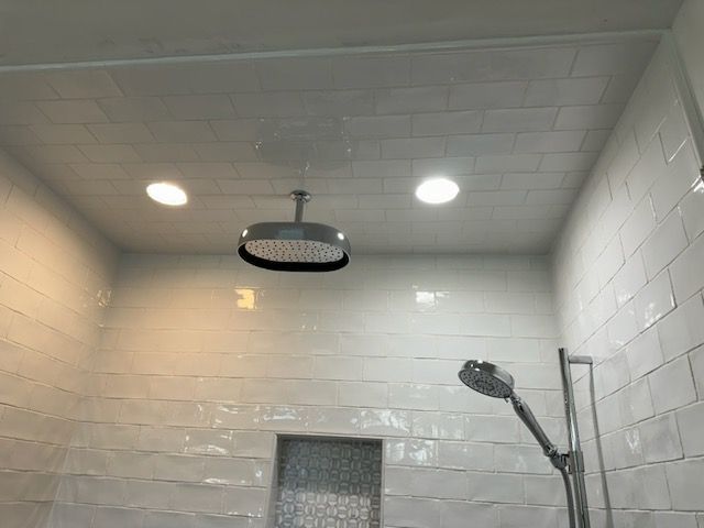 A bathroom with white tiles and a shower head hanging from the ceiling.