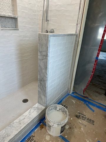 A bathroom with a shower and a bucket of paint on the floor.