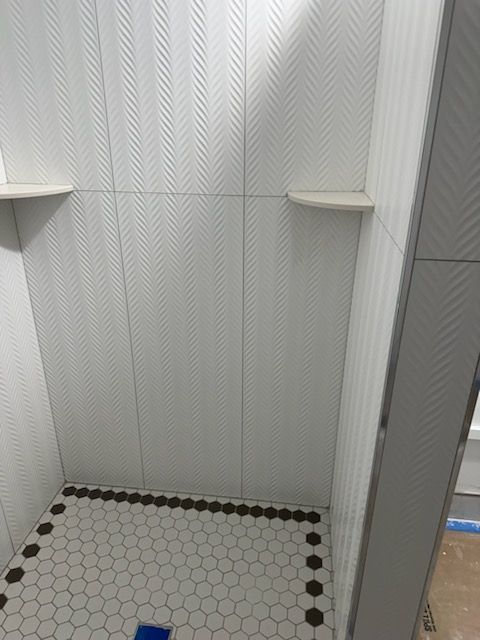 A shower with white tiles and black dots on the floor.