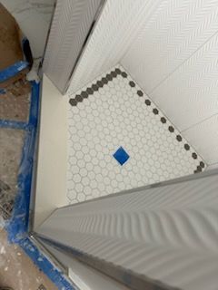 A shower stall with a hexagonal tile floor and a blue square in the middle.