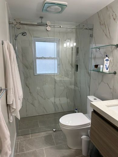 A bathroom with a toilet , sink , shower and window.