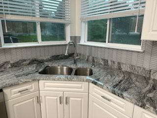 A kitchen with two sinks , white cabinets , granite counter tops and a window.