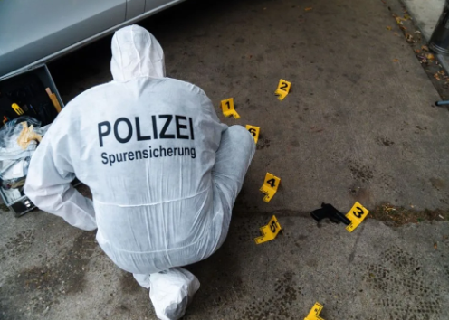 Eine Person in einem weißen Forensikanzug mit der Aufschrift „Polizei“ untersucht im Freien Beweise, die gekennzeichnet sind.