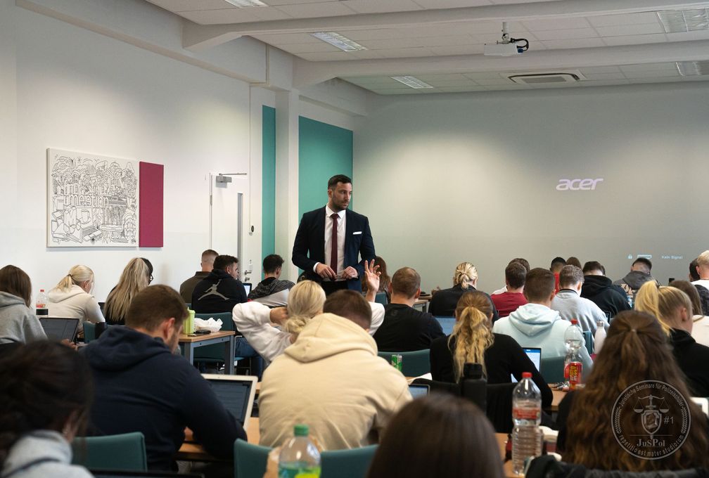 Ein Mann im Anzug hält vor einer Gruppe von Studenten in einem Hörsaal eine Präsentation.