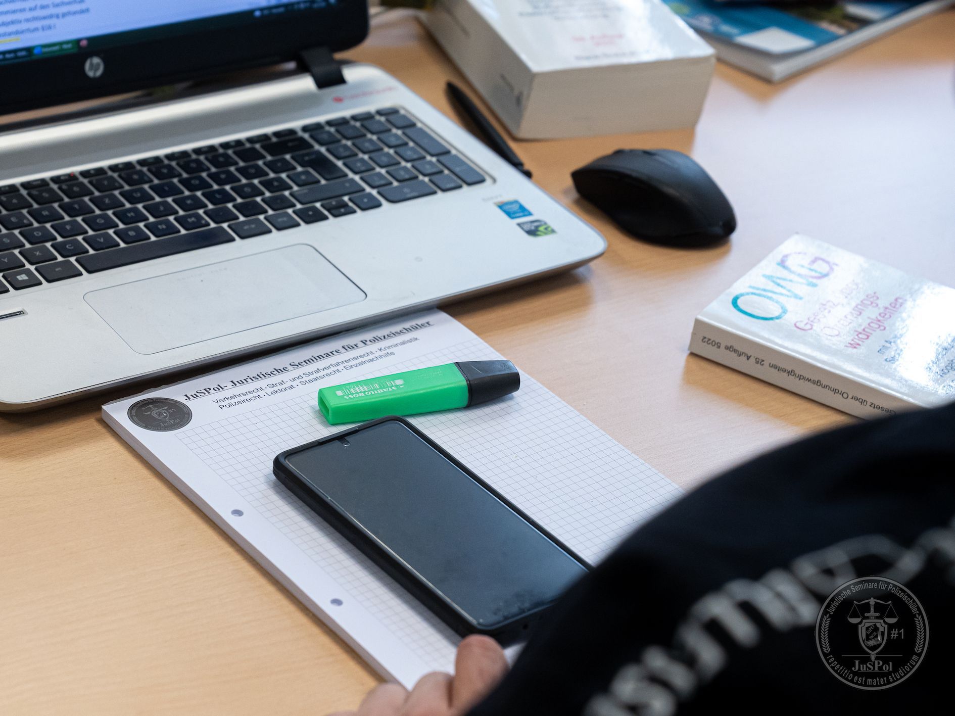 Laptop, Notizbuch, Telefon, Textmarker und Buch auf einem Schreibtisch.