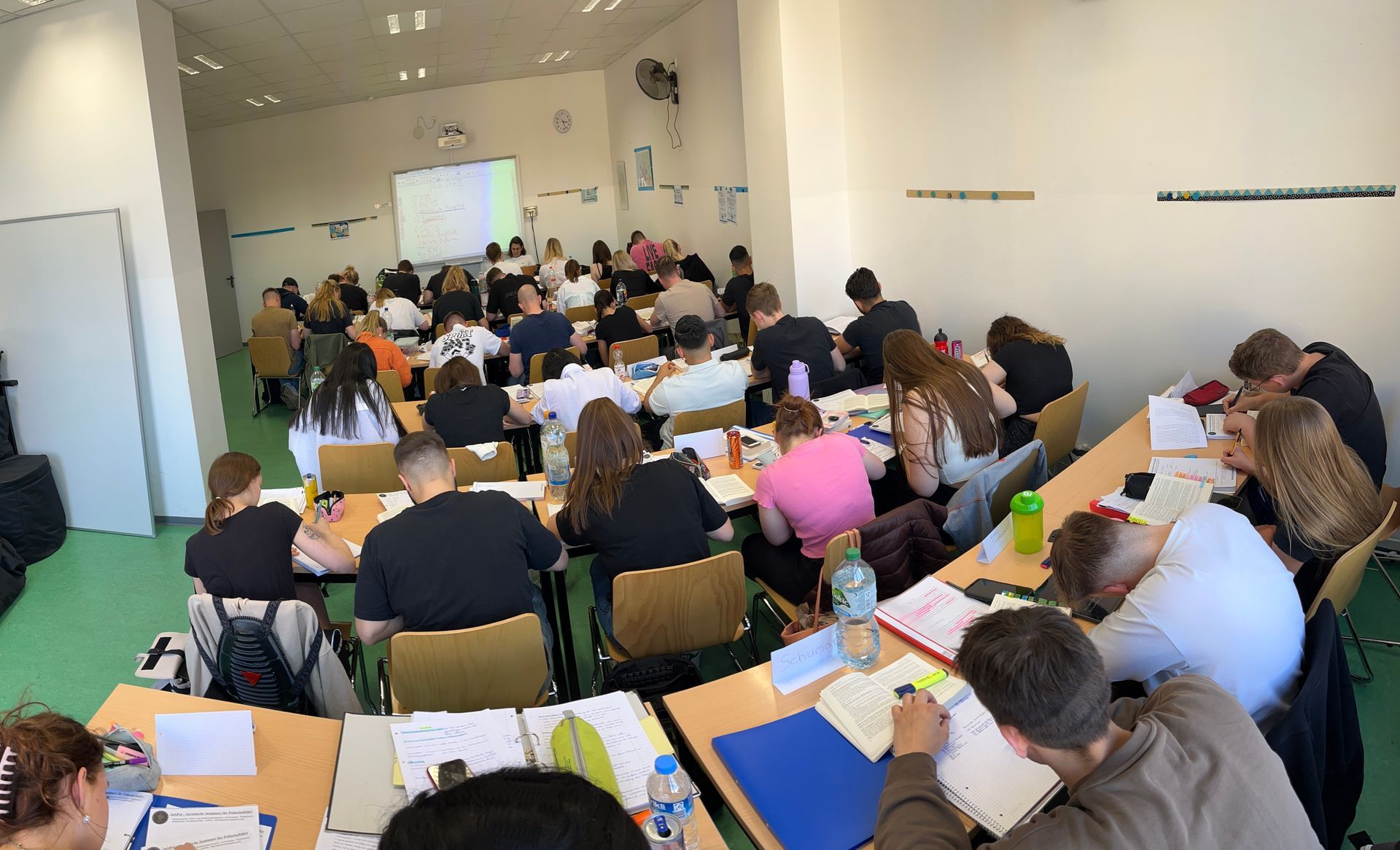Klassenzimmer mit Schülern, die vor einer Projektionsleinwand Notizen machen.