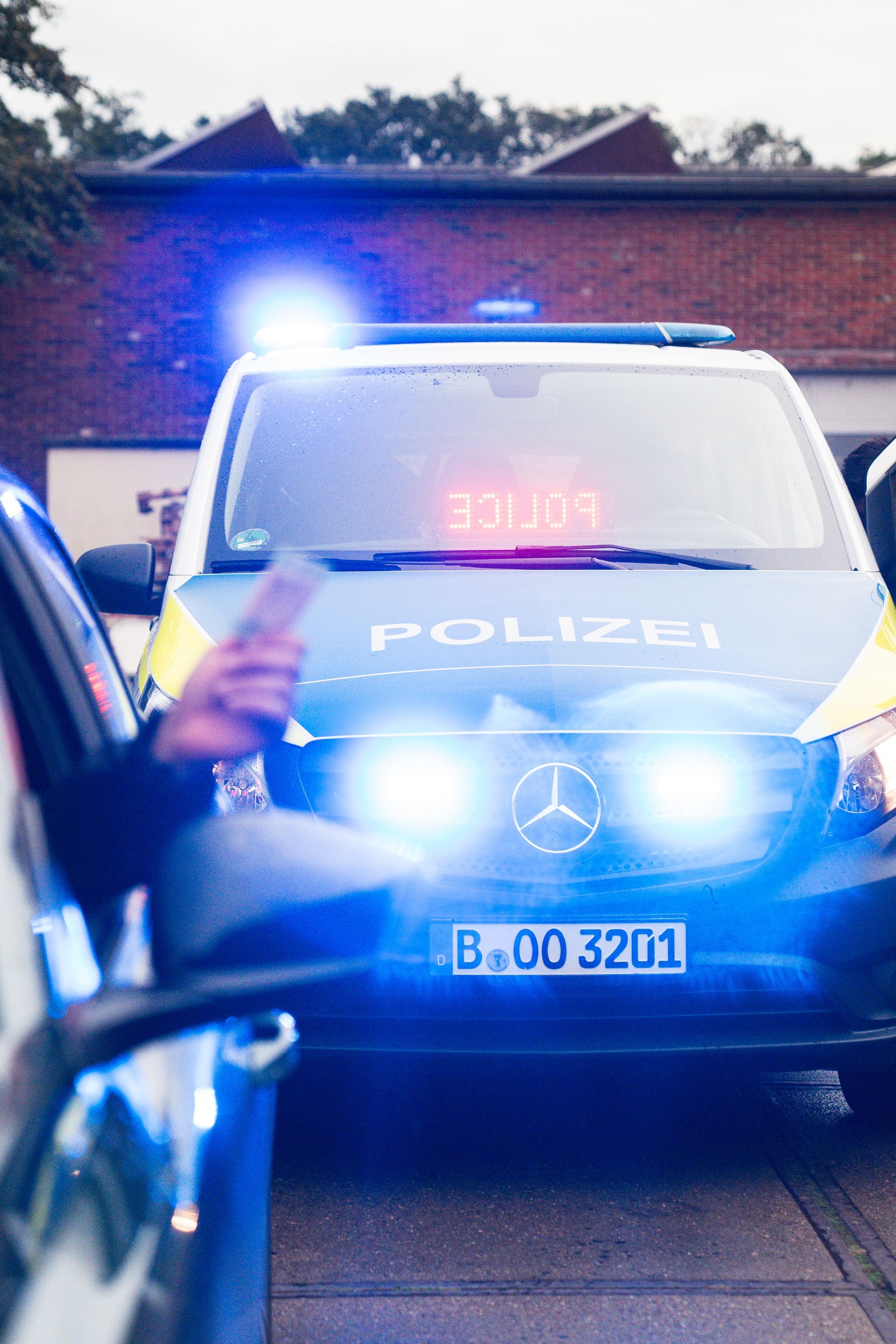 Eine Person wird von einem deutschen Polizeiauto angehalten. Blaulicht blinkt.