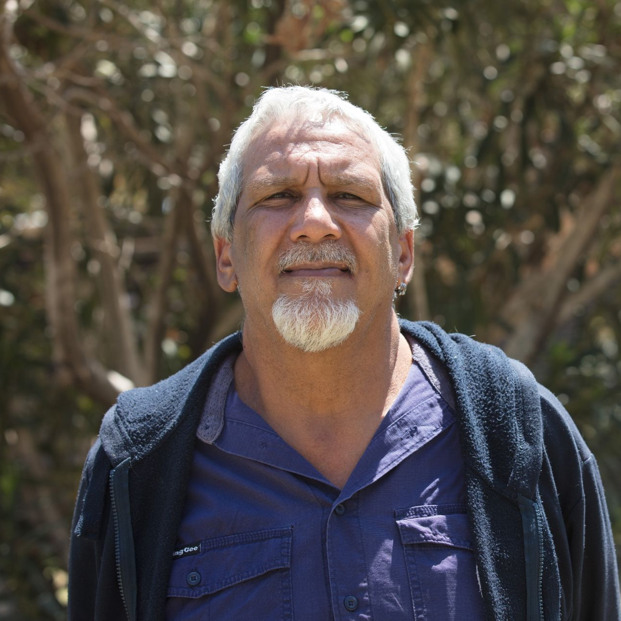 Man with gray hair and goatee in a blue shirt and jacket, standing outdoors, looking at the camera.