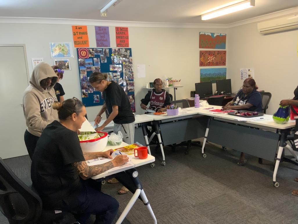 People preparing food at a table in a brightly lit room with posters on the walls.