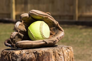 Baseball glove with ball on green grass, with blurred baseballs in the background.