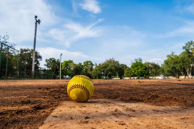 Baseball glove with ball on green grass, with blurred baseballs in the background.