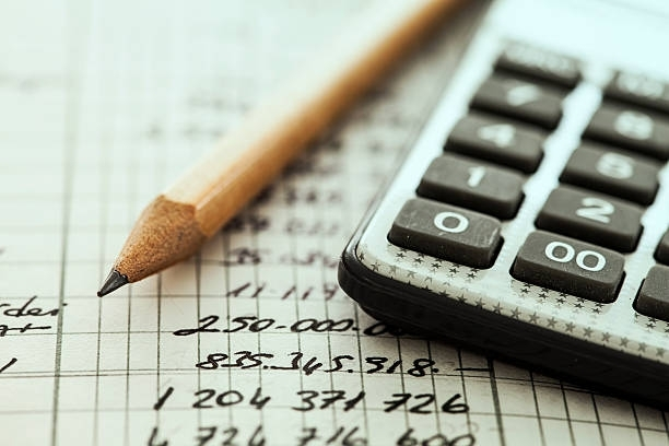 Close-up of a list of numbers written on a piece of paper, with a pencil and calculator on top.