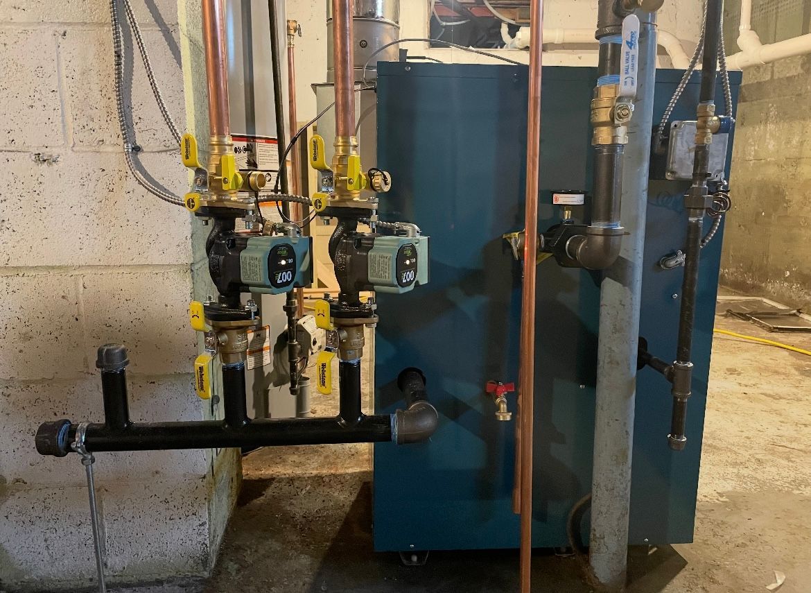 Blue boiler and associated pipes and pumps in a basement setting.