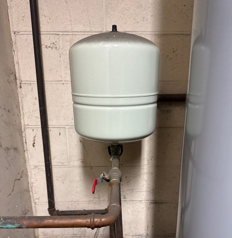 Light green thermal expansion tank connected to copper pipes, mounted on a brick wall.
