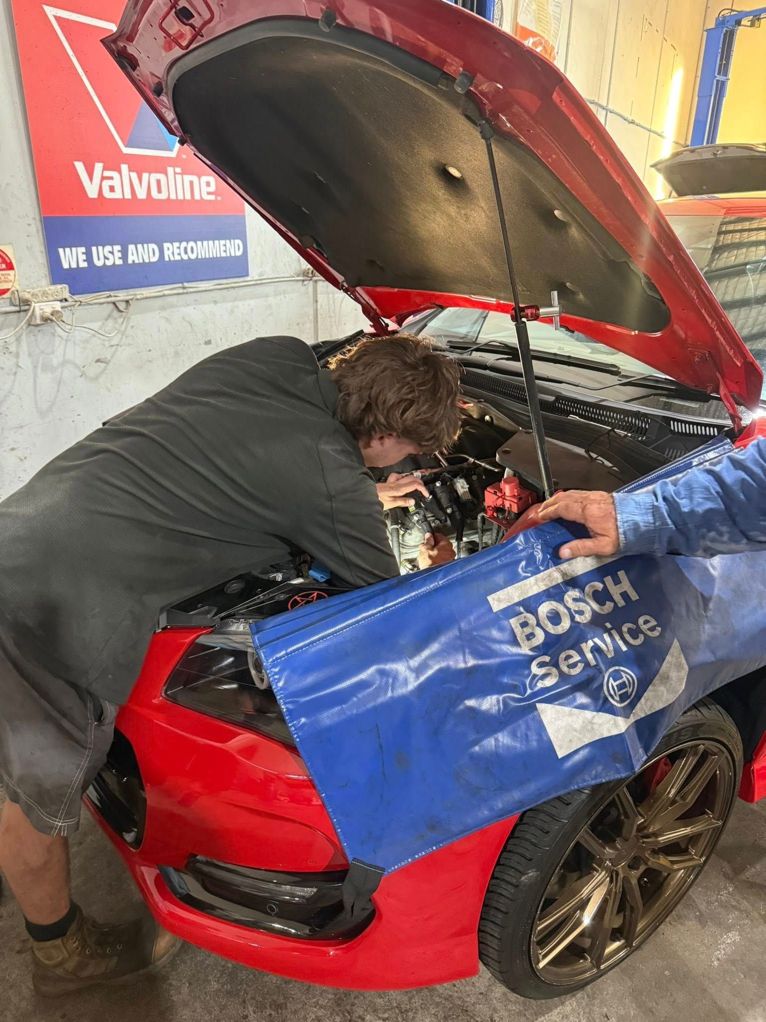 Mechanic working under the hood of a red car in a garage — Elite Fleet Auto in Cannonvale, QLD