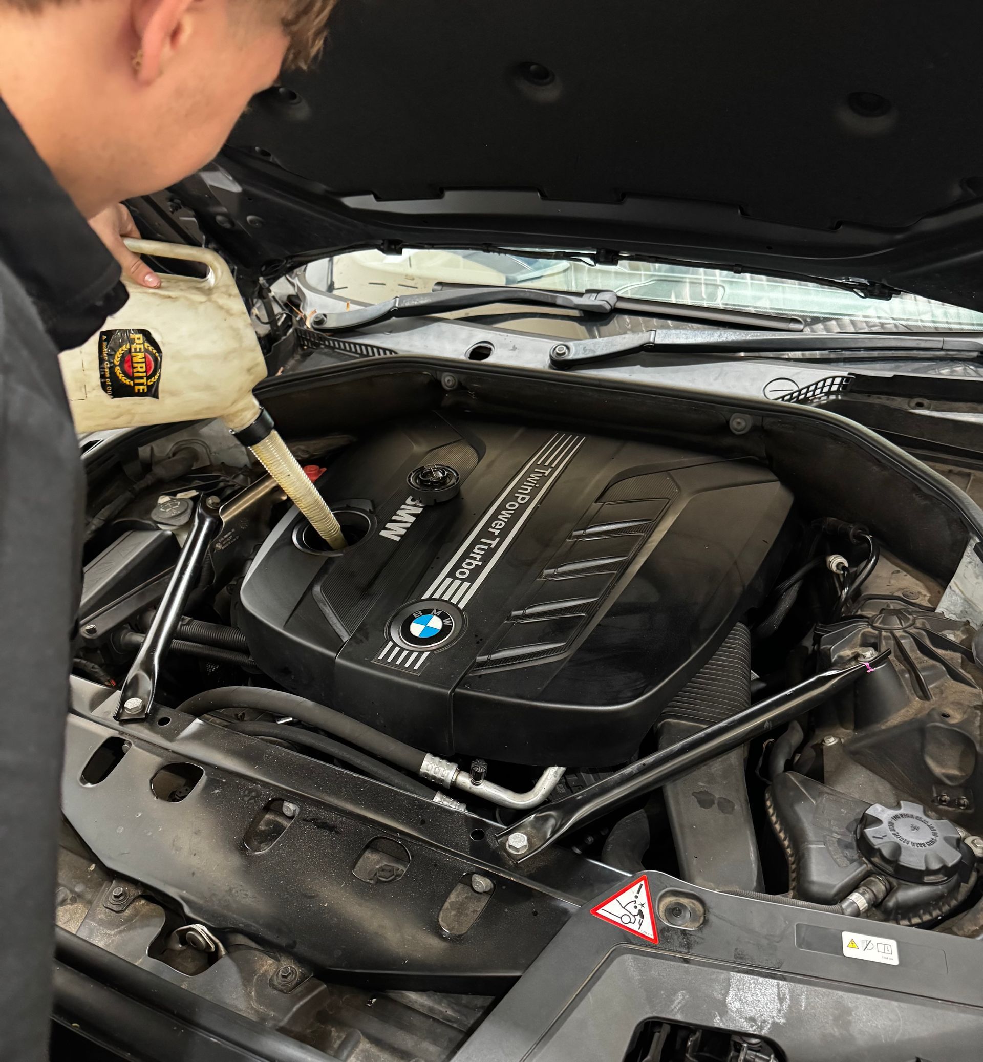 Mechanic pouring fluid into a BMW engine bay under an open hood — Elite Fleet Auto in Cannonvale, QLD