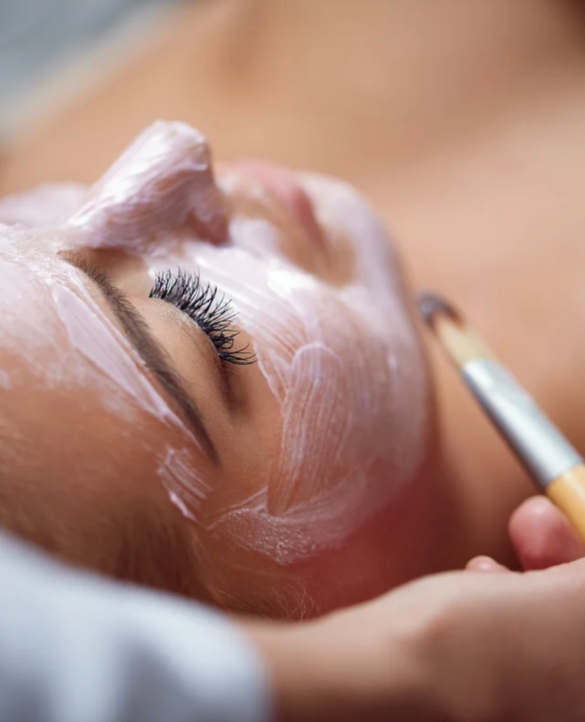 A woman is getting a facial treatment with a brush.