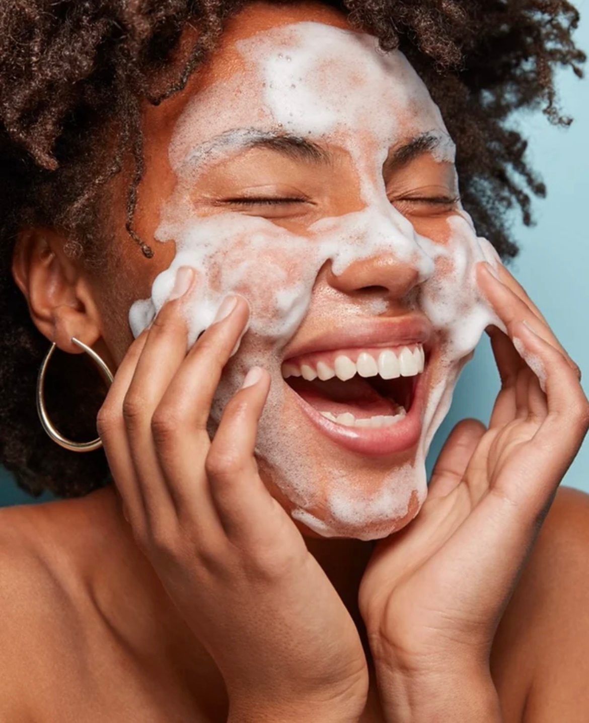 A woman is washing her face with soap and smiling.