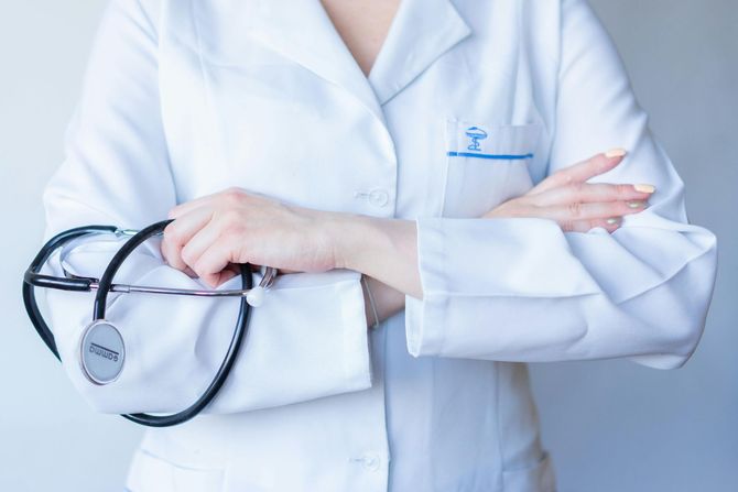 A healthcare professional in a white coat with arms crossed, holding a stethoscope.