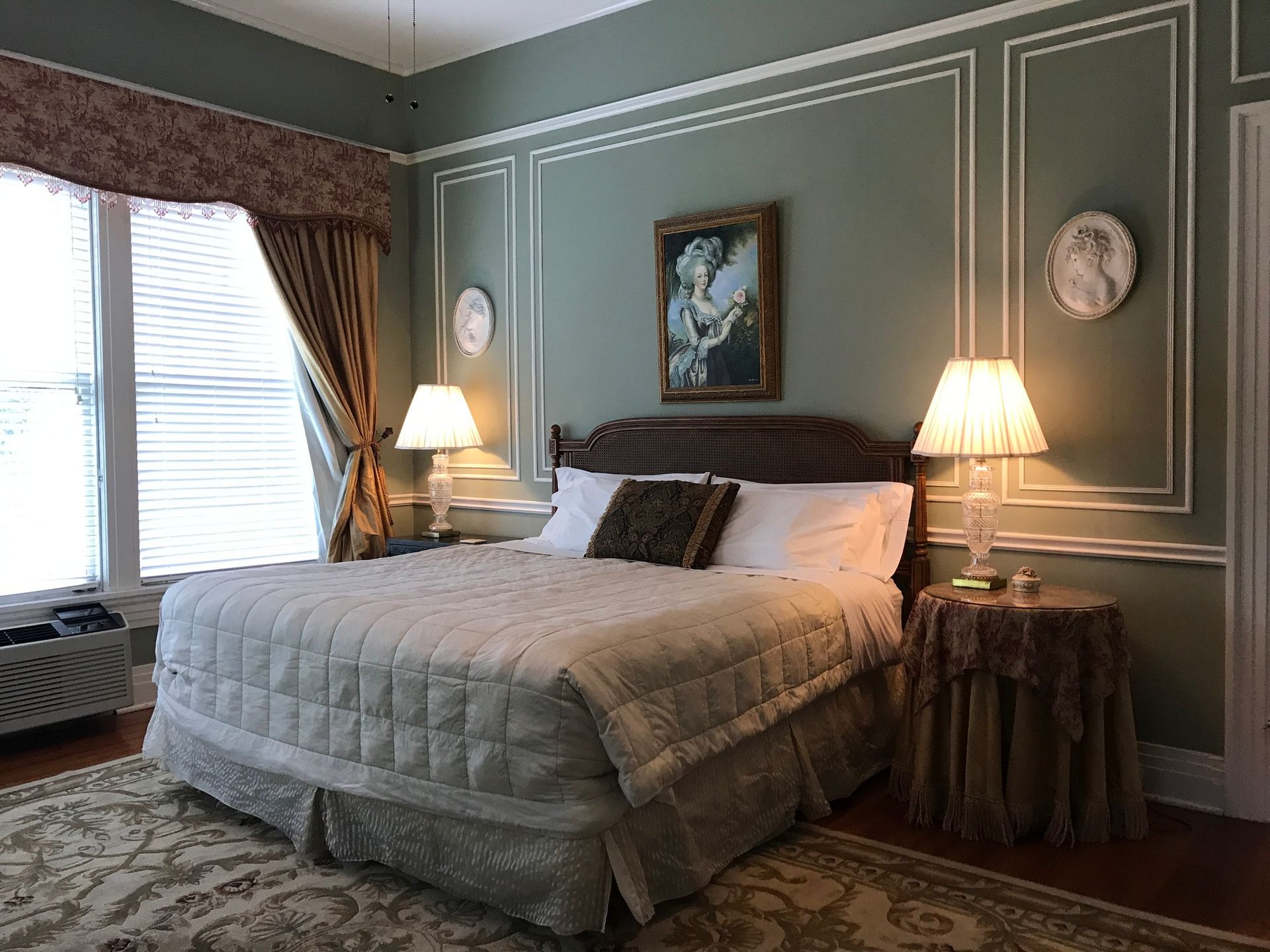 A bedroom with a king size bed , two lamps , a rug and a painting on the wall.