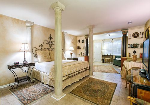 A bedroom with a king size bed surrounded by columns and a rug.