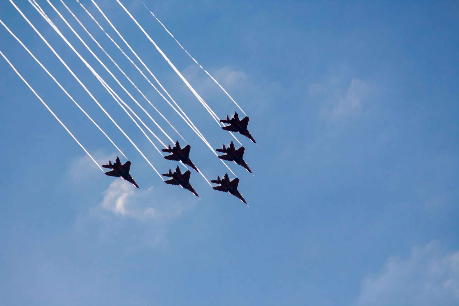 Six fighter jets flying in formation, leaving white contrails against a blue sky.