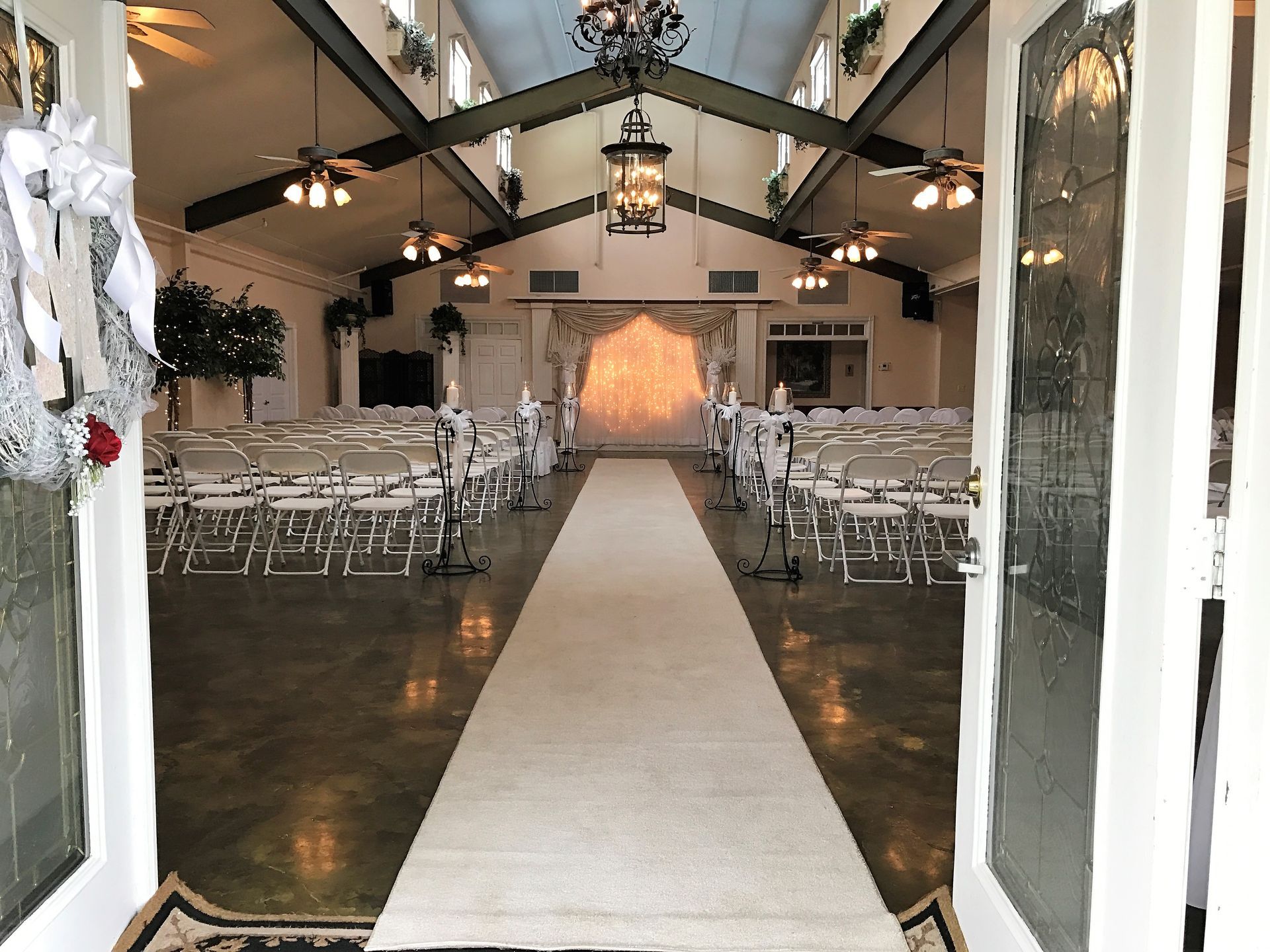 The aisle of a wedding ceremony is lined with white chairs and a white carpet.