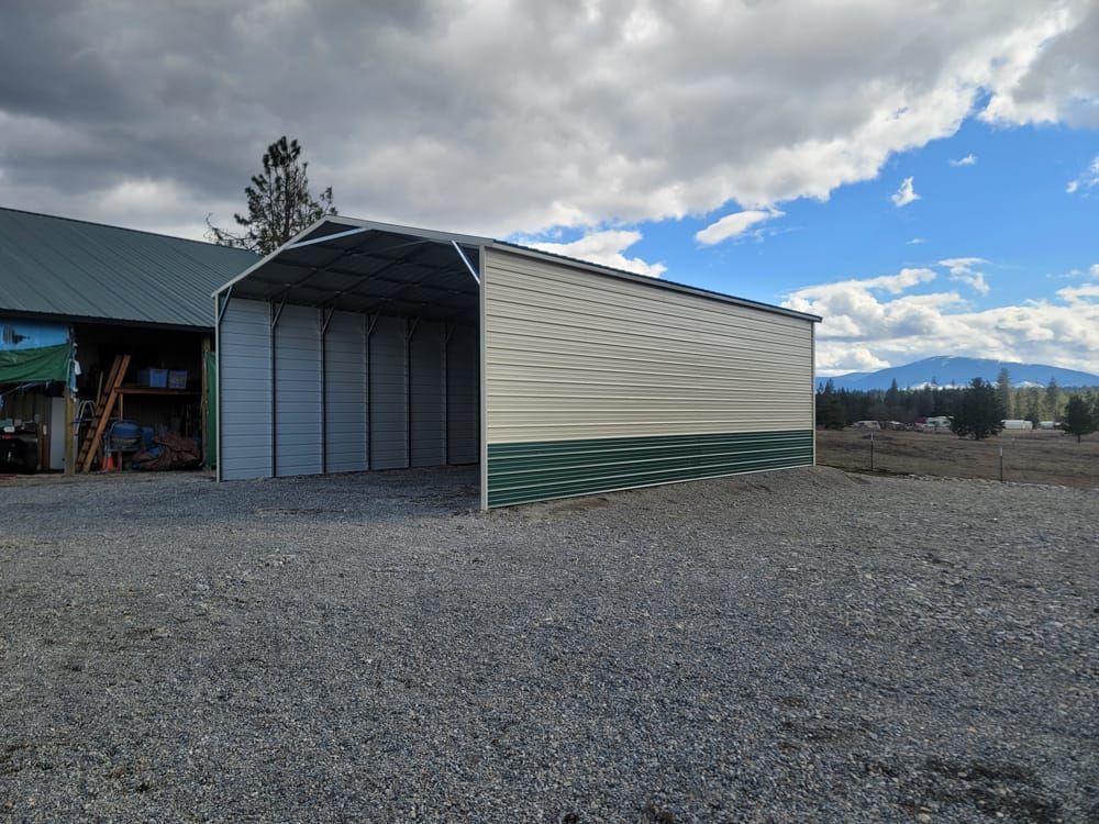A large metal building is sitting in the middle of a gravel lot.