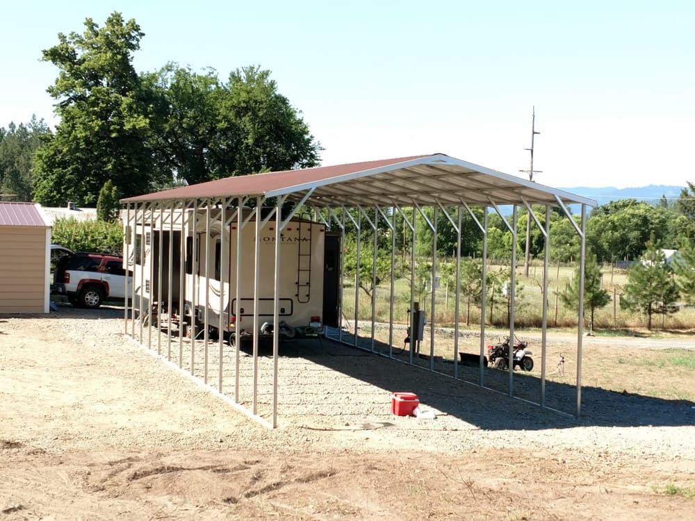 A trailer is parked under a canopy in a dirt field.
