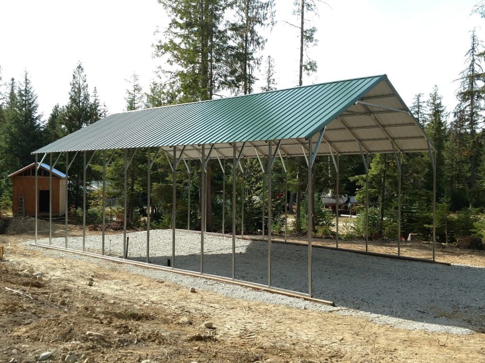 A carport with a green roof is sitting on top of a gravel road.