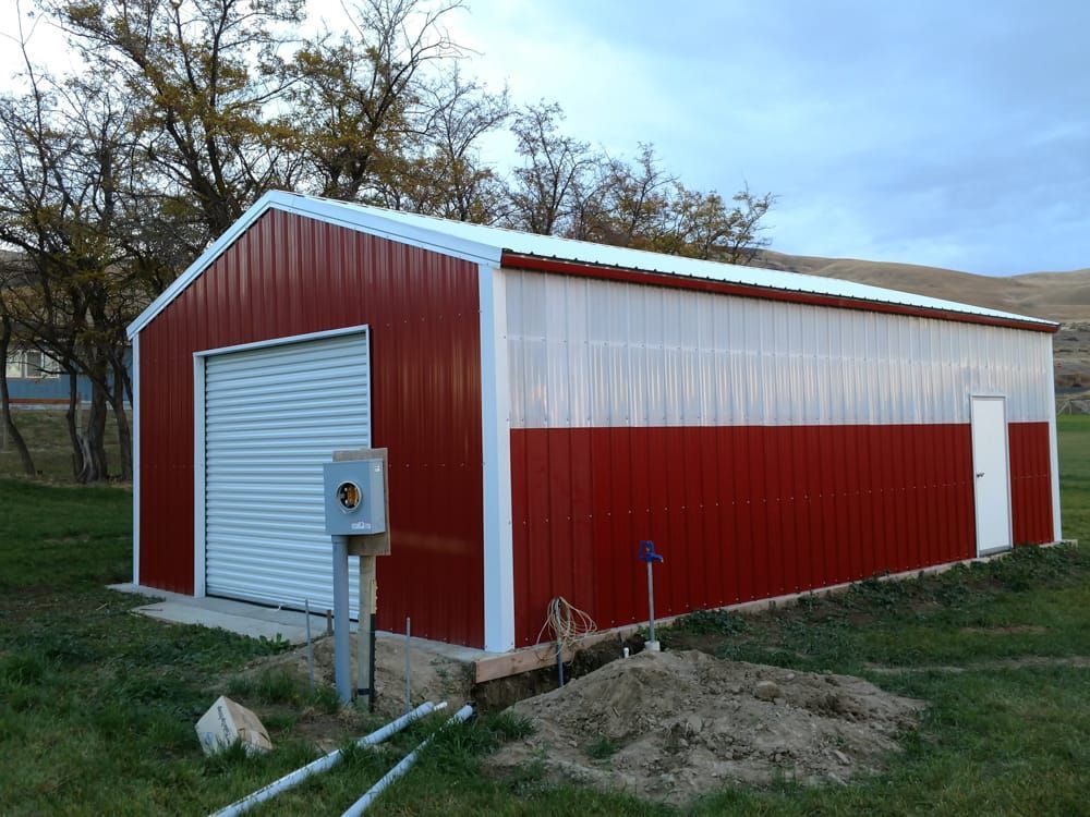 A red and white barn with a white roof is sitting in the middle of a grassy field.