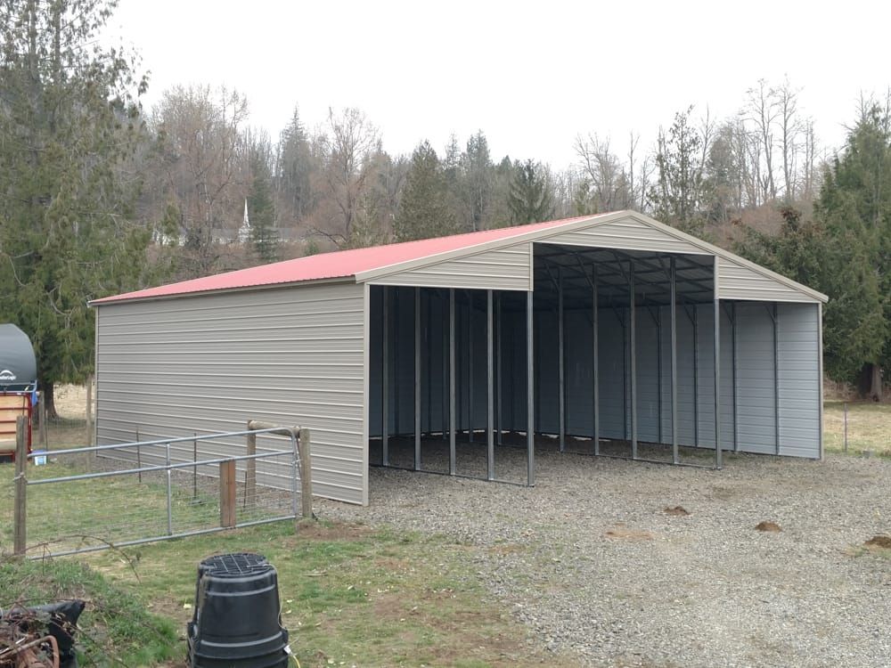 A large metal building with a red roof is in a gravel area.