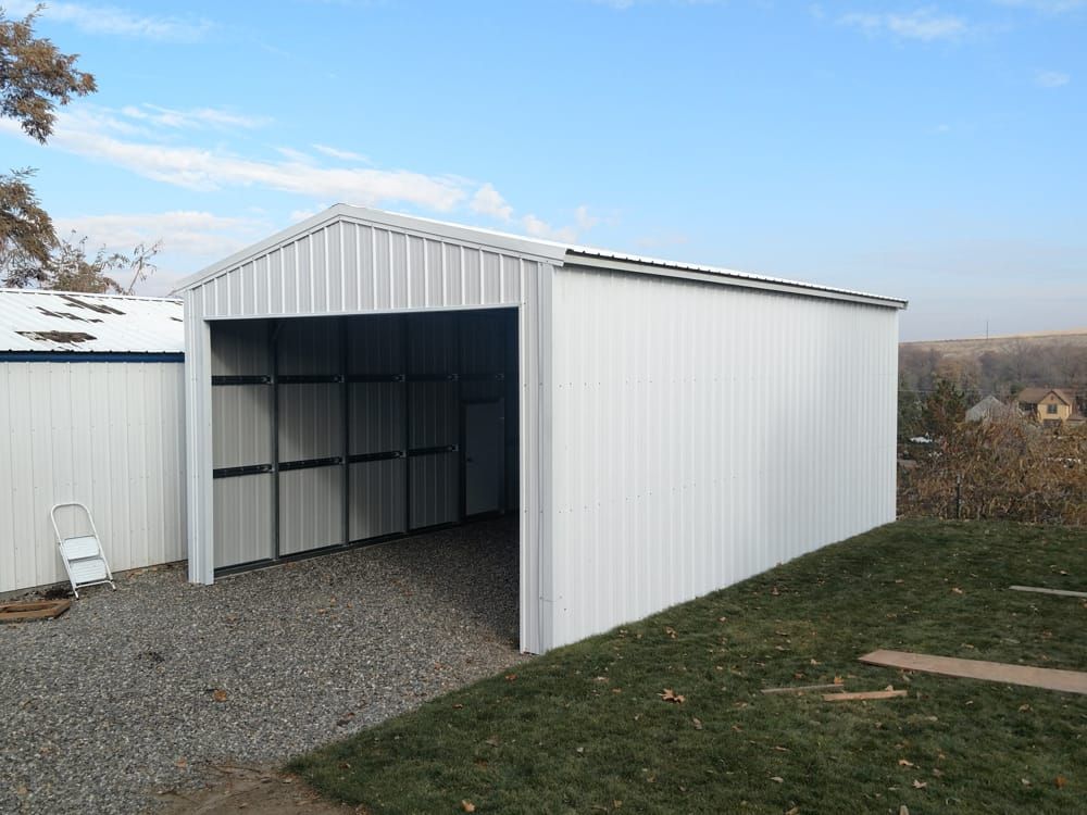 A white metal garage is sitting in the middle of a grassy field.
