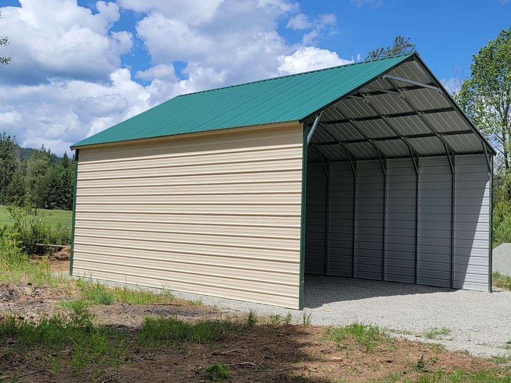 A metal building with a green roof is sitting in the middle of a field.