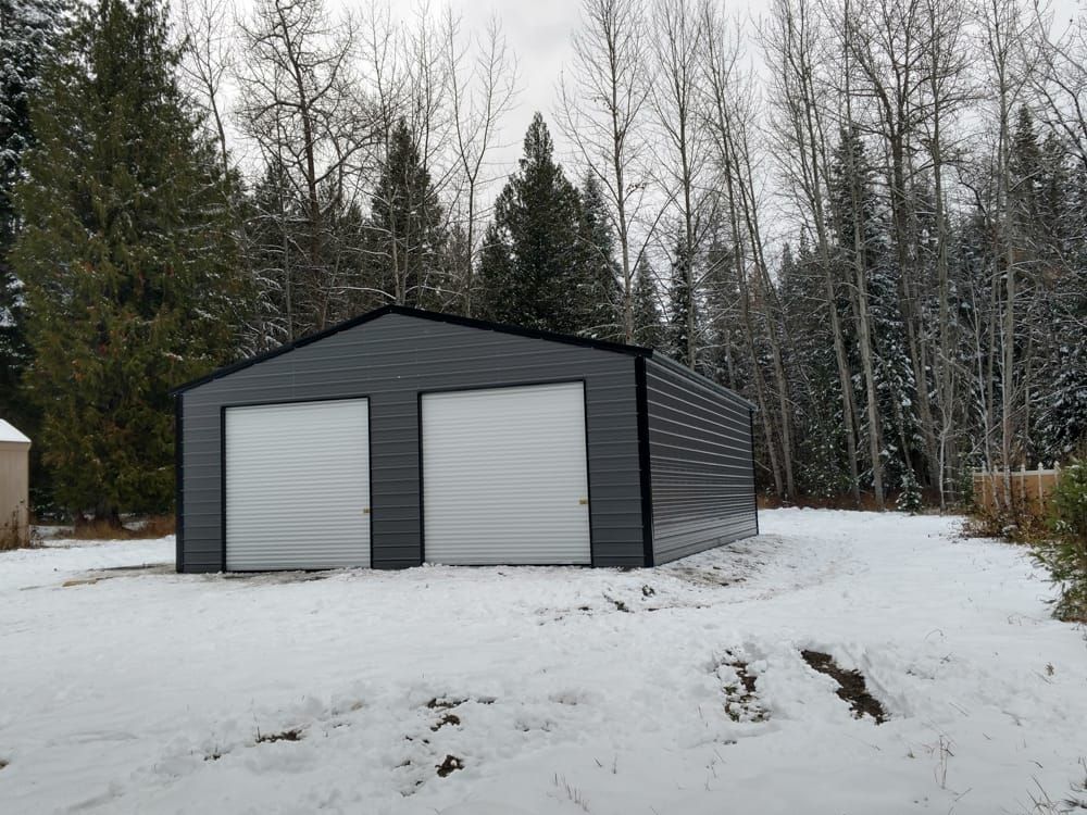 A metal garage is sitting in the middle of a snow covered field.