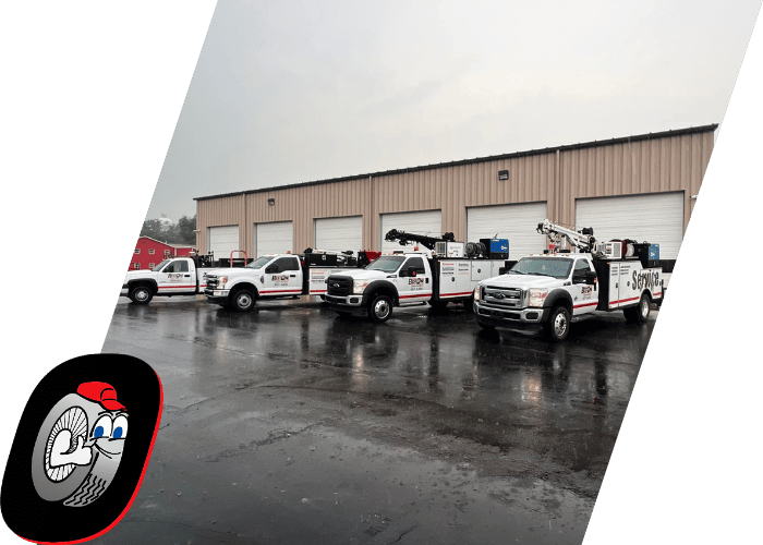 Fleet of utility service trucks parked outside a commercial repair facility on a rainy day.