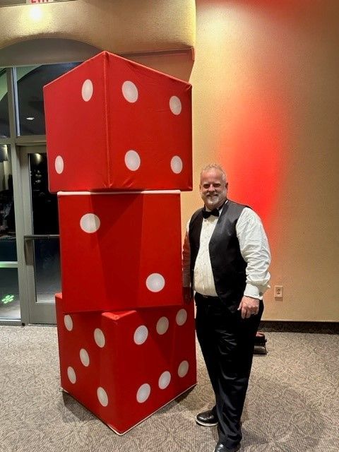 A man in a tuxedo is standing next to a stack of red dice decor.