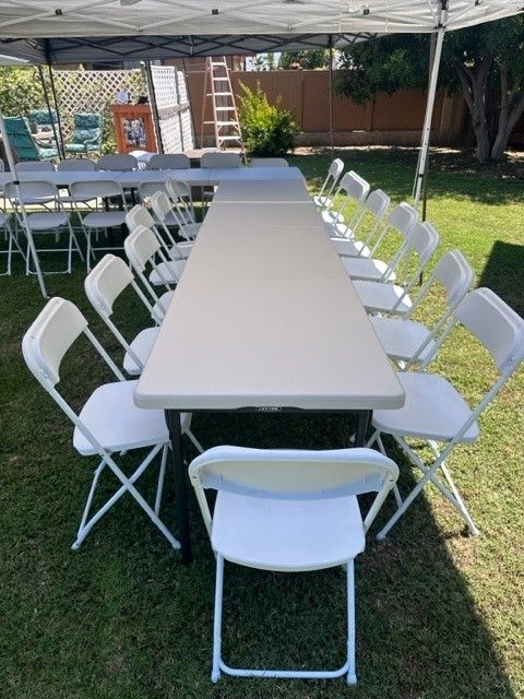 A long table with white folding chairs under a tent.